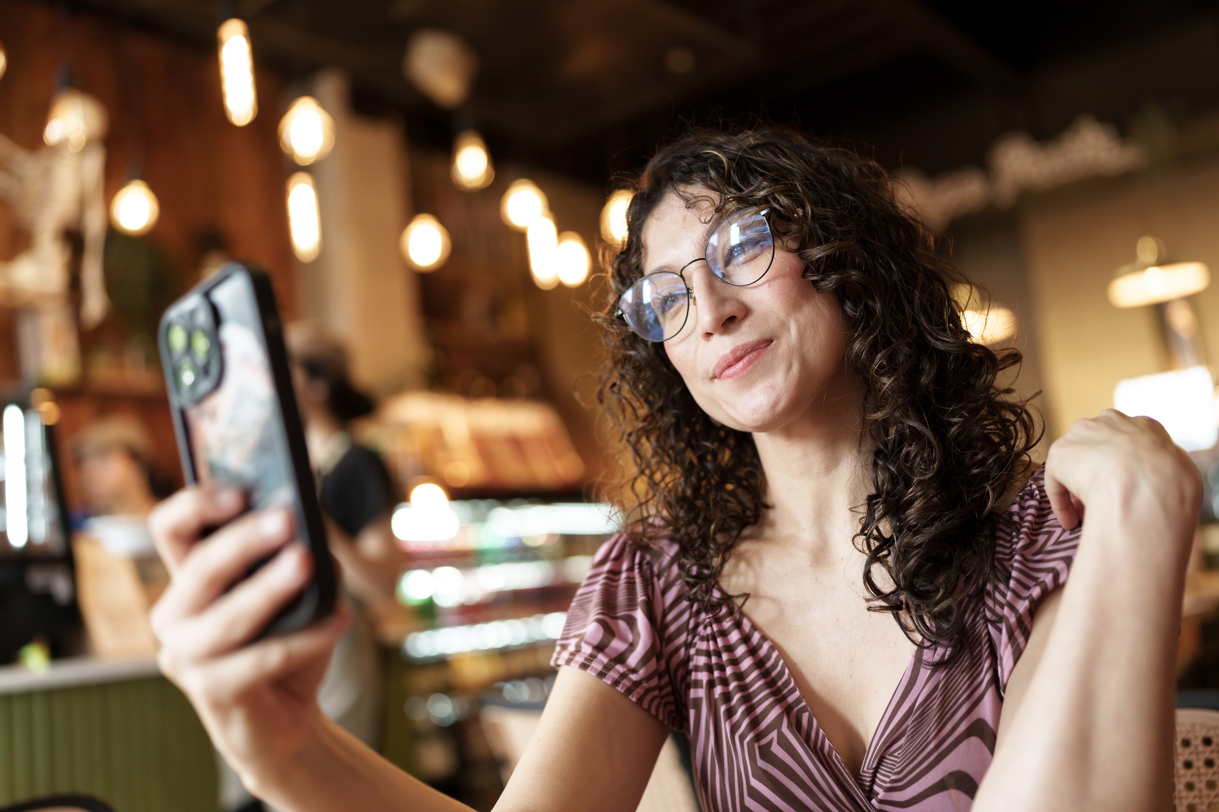 Woman with glasses taking a selfie with a smartphone in a restaurant setting