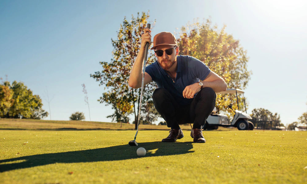 Man on a golf course wearing sunglasses preparing to take a shot with a golf club.