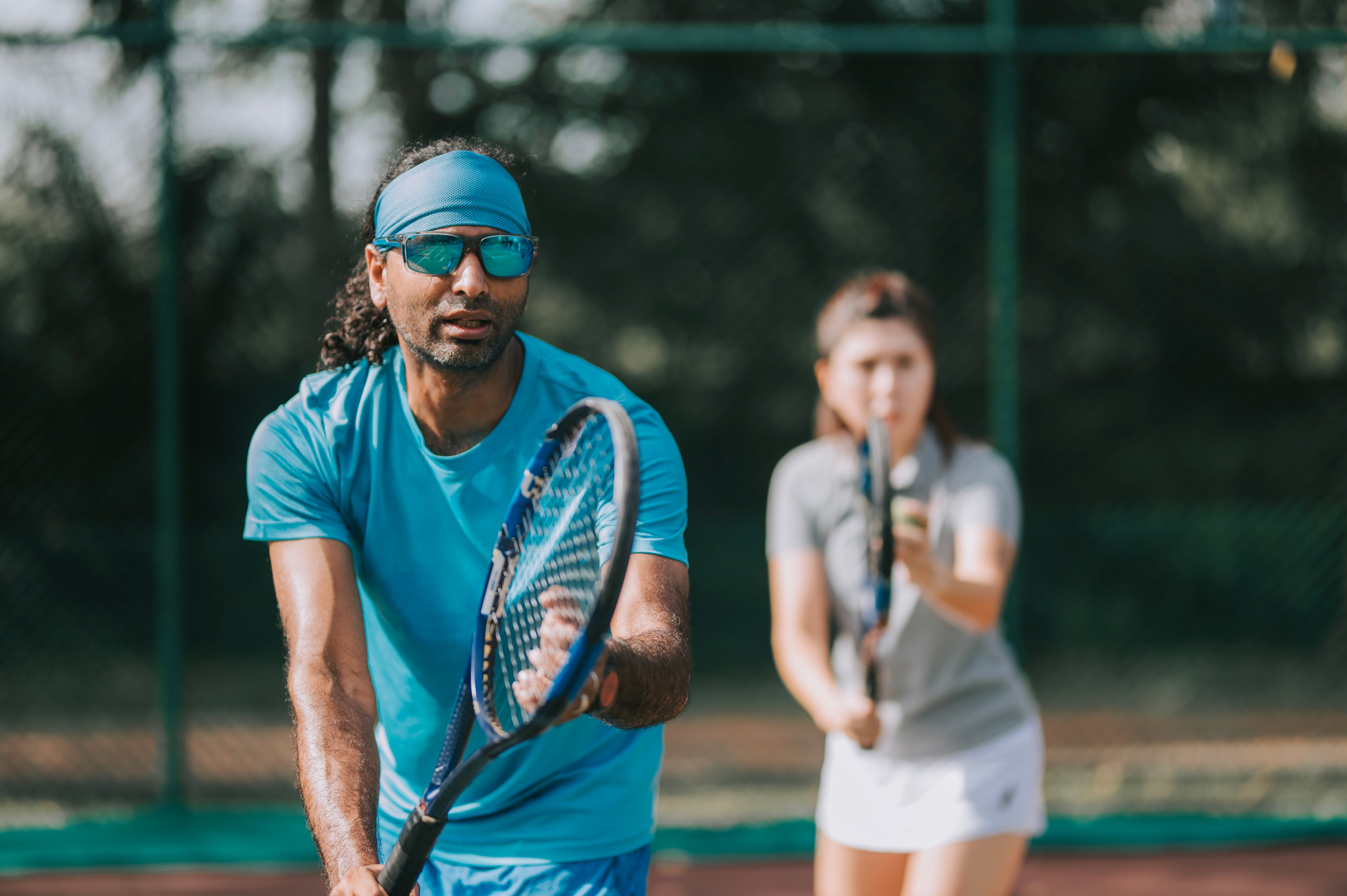 Two tennis players on a court, one in blue and one in gray, with a blurred background.