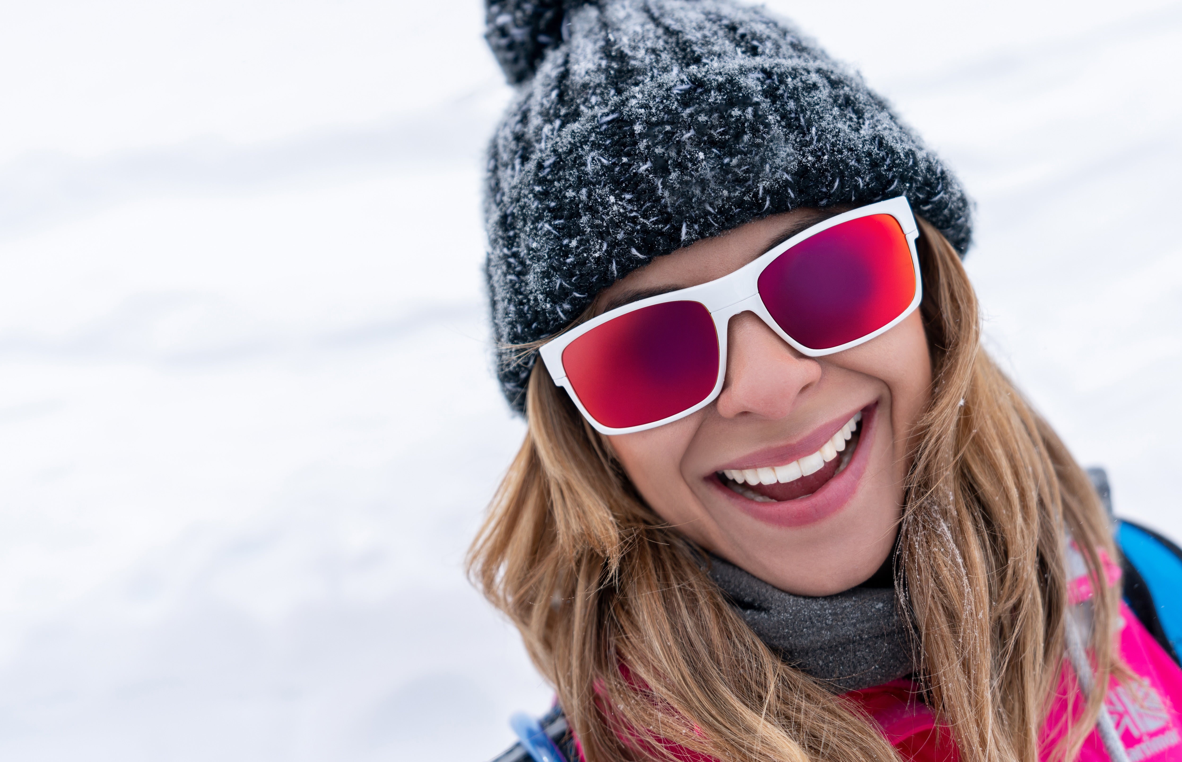 Person wearing a dark knit hat and red sunglasses with a snowy background