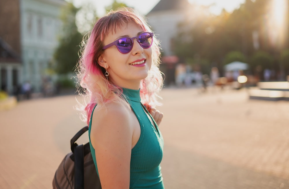 Woman with pink hair wearing sunglasses and a green top, standing outdoors.