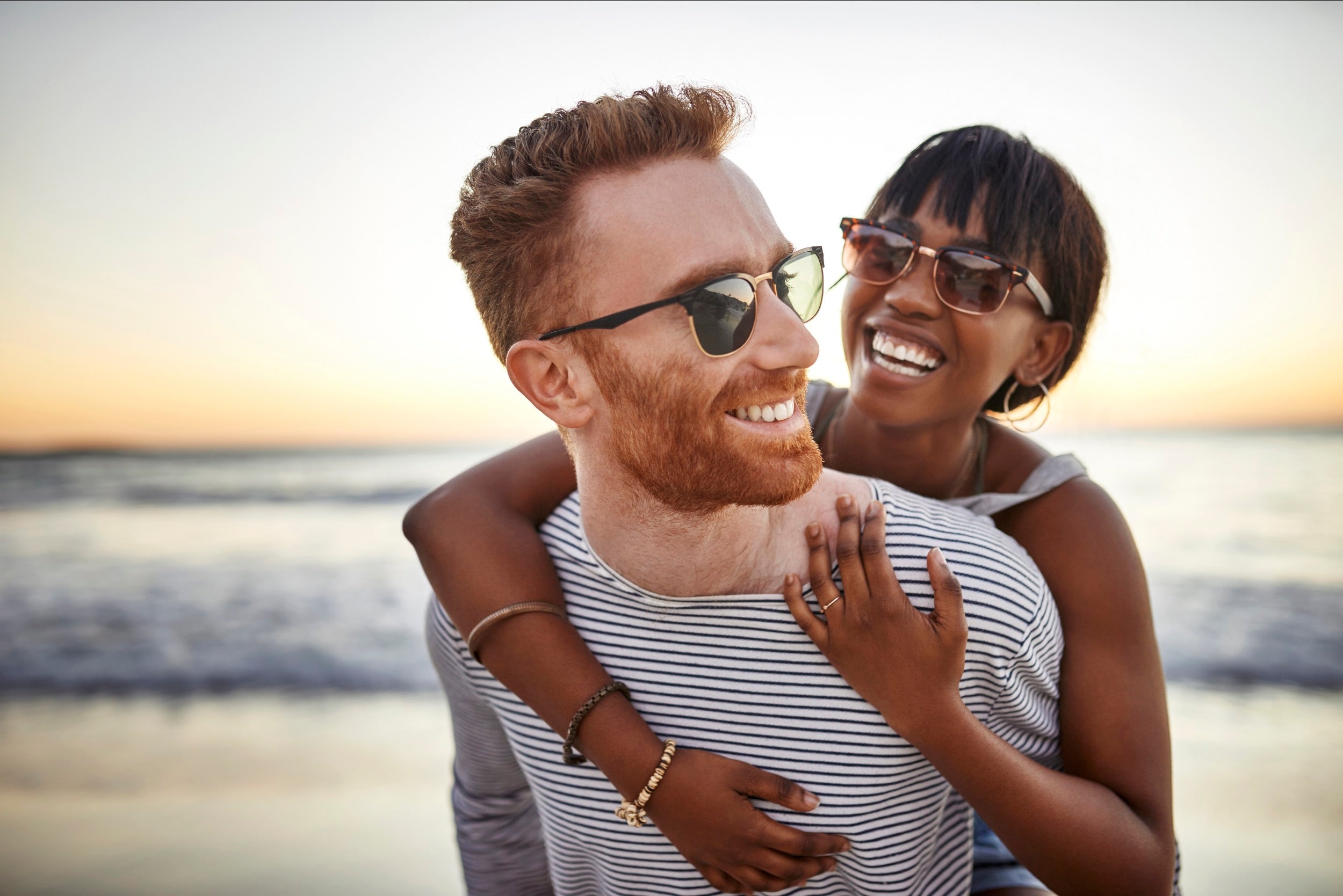 Couple embracing on a beach at sunset wearing sunglasses