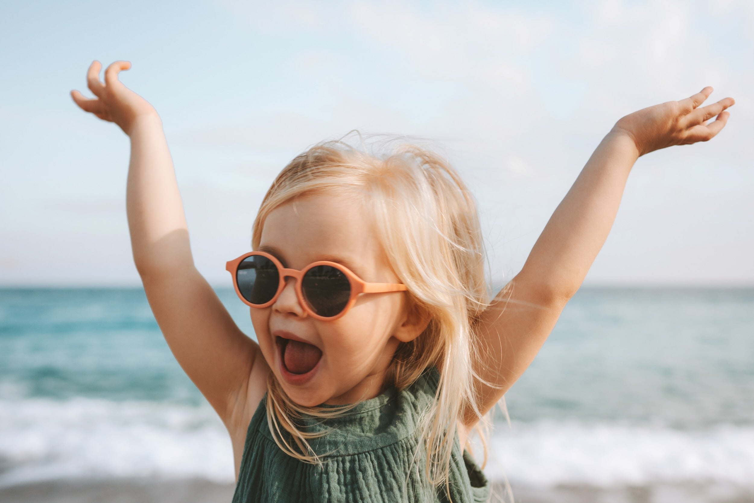 Child wearing sunglasses with arms raised on a beach